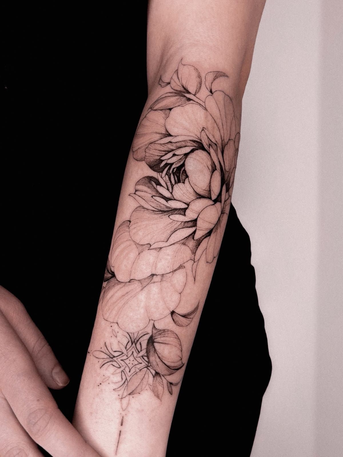 Fine-Line-Blüten, die sich um den Unterarm legen, darunter ein feines Ornament