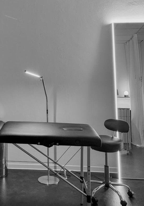 Behandlungsliege mit Arbeitsleuchte und Hocker vor dem beleuchteten Spiegel