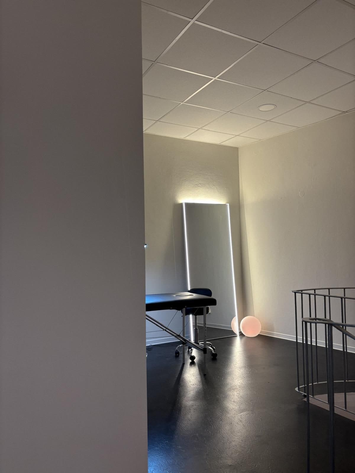 Blick durch den Türdurchgang auf Behandlungsliege, beleuchteten Spiegel und Kugelleuchte