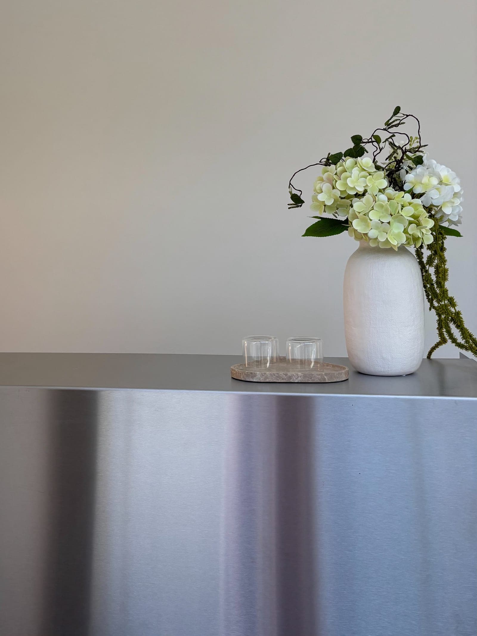 Blumenstrauß in heller Vase auf der Chromtheke, daneben zwei Gläser auf einem Marmortablett